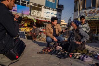 An online producer talks to an older man selling shoes on the street in Kabul