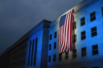 Image of an American flag hanging off the side of a building that is awash in dark blue lighting.