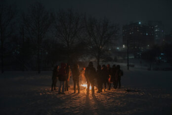 Photo of a group of people gathered in a circle around a fire put, after sundown.