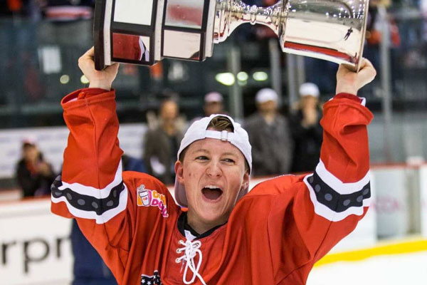 Photograph shows a hockey player holding a trophy aloft on the rink