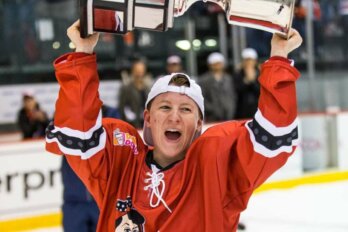 Photograph shows a hockey player holding a trophy aloft on the rink