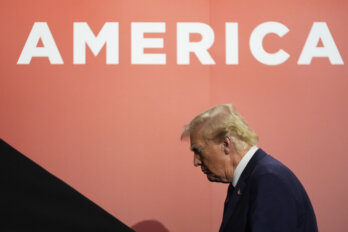 A photo of Donald Trump with his head bowed. Above him is a wall that reads America.