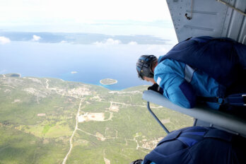 A photograph of skydivers waiting at the edge of an open helicopter door before making the jump.
