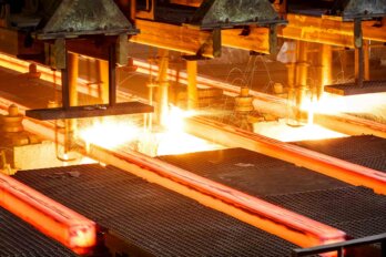 Photo shows close shot of hot steel on conveyor in a steel mill