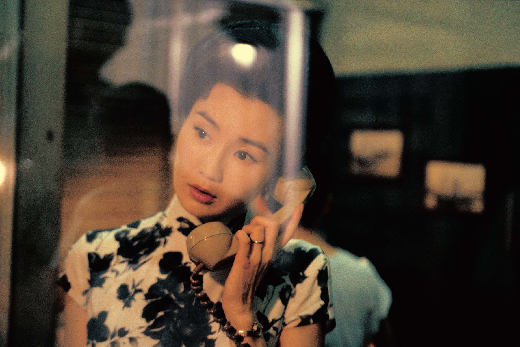 A woman holds the receiver of a rotary phone while gazing out the window in a still from In the Mood for Love.