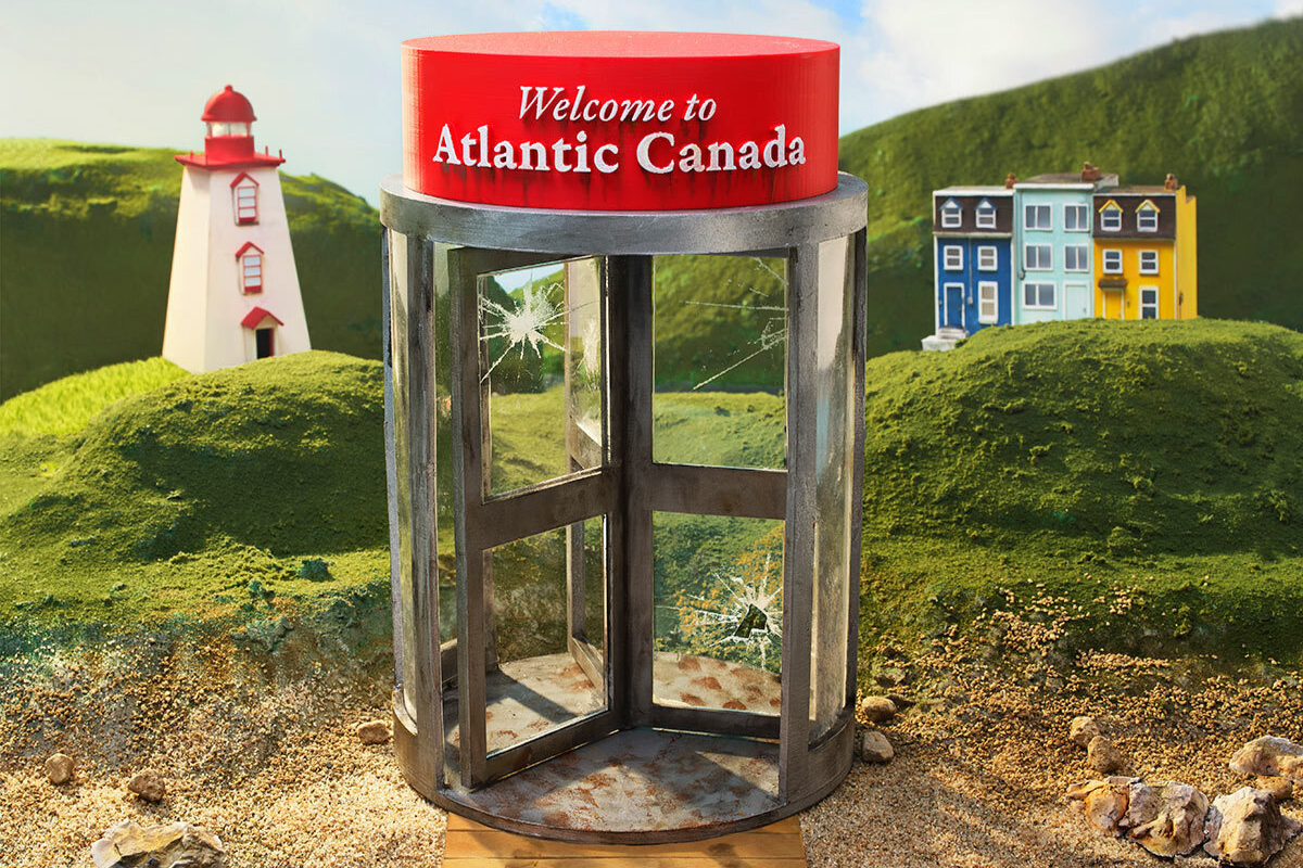 In an illustration, a boardwalk with footprints connects to a sandy shore and rolling green hills with a lighthouse and a colourful cluster of buildings. On top of a revolving door with broken windows is a sign that reads Welcome to Atlantic Canada.