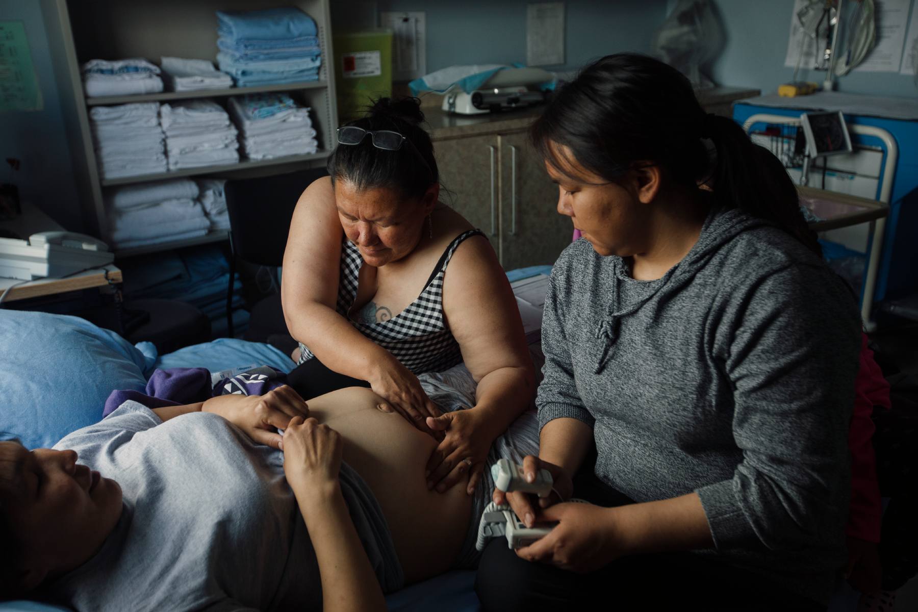 Photo of two women sitting with a pregnant person. One of the women is touching her belly.