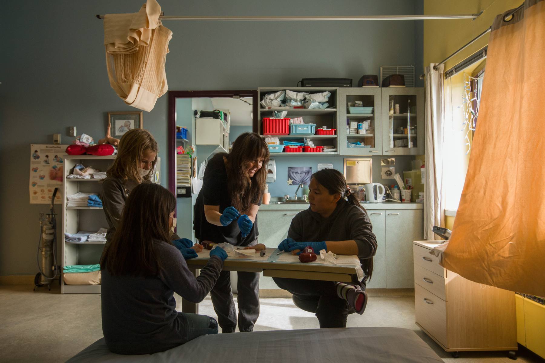 Image of four people around a table. One of the people is giving a demonstration while wearing blue medical gloves.