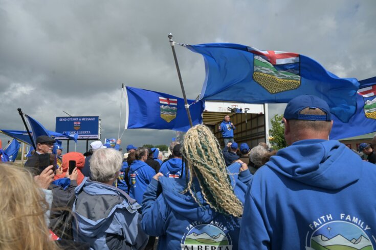 Photo of a crowd of people wearing blue hoodies and waving Alberta provincial flags.