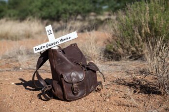 A brown leather knapsack leans against a white cross in the desert