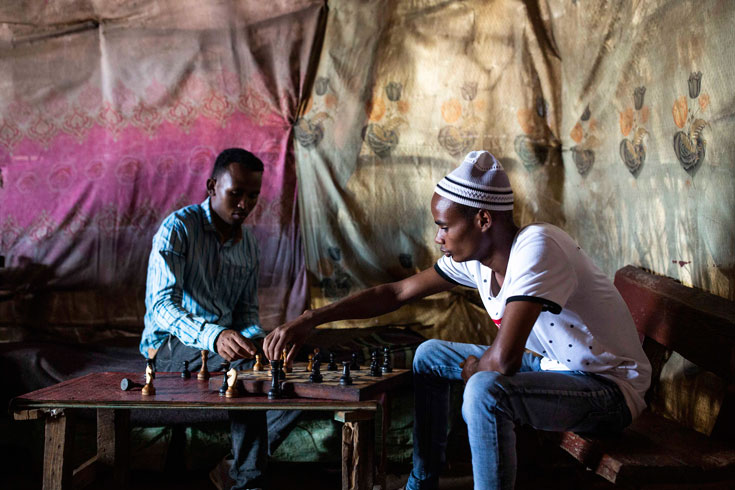 Two men play chess inside an Ethiopian restaurant, the walls covered by patterned cloths..