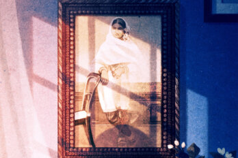 An illustration of a woman's shadow casting over a framed photograph of a young woman wearing Mughal-era clothing, bangles, rings, and jasmine flowers