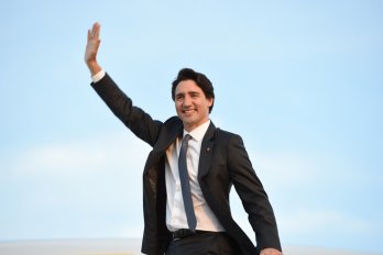 Justin Trudeau wearing a suit and waving against the backdrop of a blue sky.