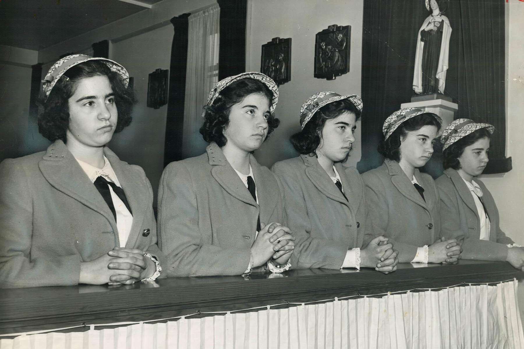 A black-and-white photo of the Dionne quintuplets, five identical teenage sisters, hands folded while kneeling in a pew