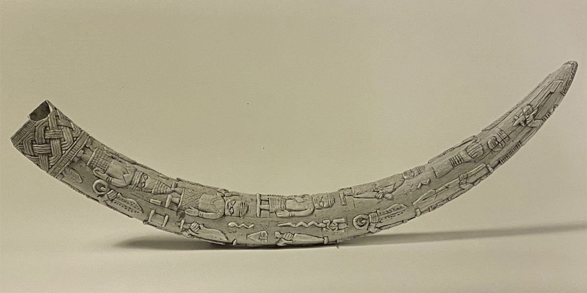 Black and white photo of an ivory elephant tusk carved with human figures and symbolic imagery.