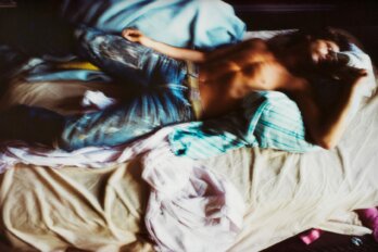 Blurred image of a man in jeans with a bare chest lying on a bed.