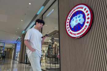 A man in a white T-shirt walks by a store with the "Canada Goose Arctic Program" logo on the wall in a shopping mall