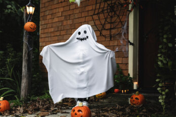 Halloween decorations, including a smiling ghost, jack-o’-lanterns, and a spider web, adorn the front of a house.