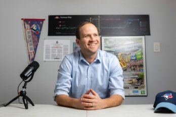 Photo of politician Nate Erskine-Smith sitting at a desk with a microphone and Toronto Blue Jay's hat.