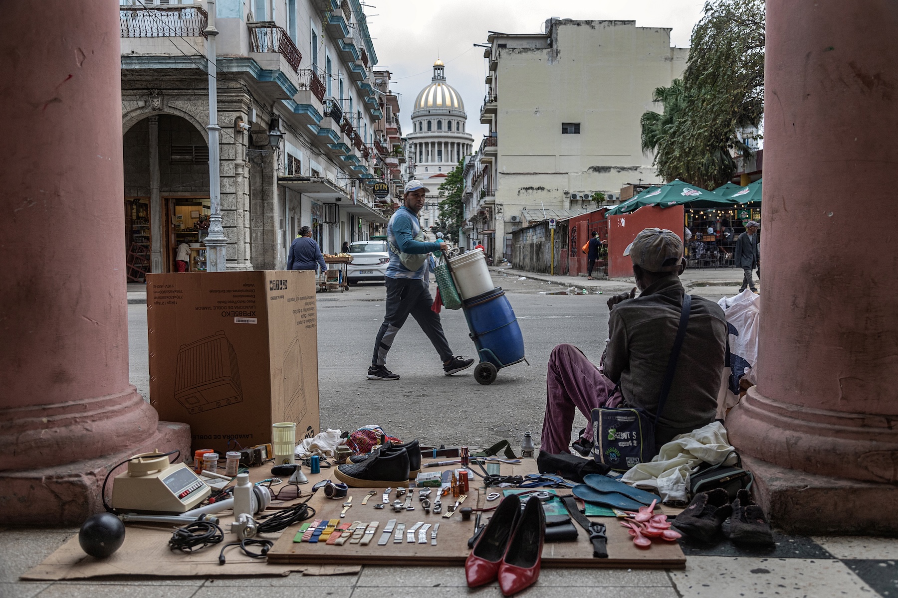 A photo of a man sitting on the ground with items lined up on cardboard.