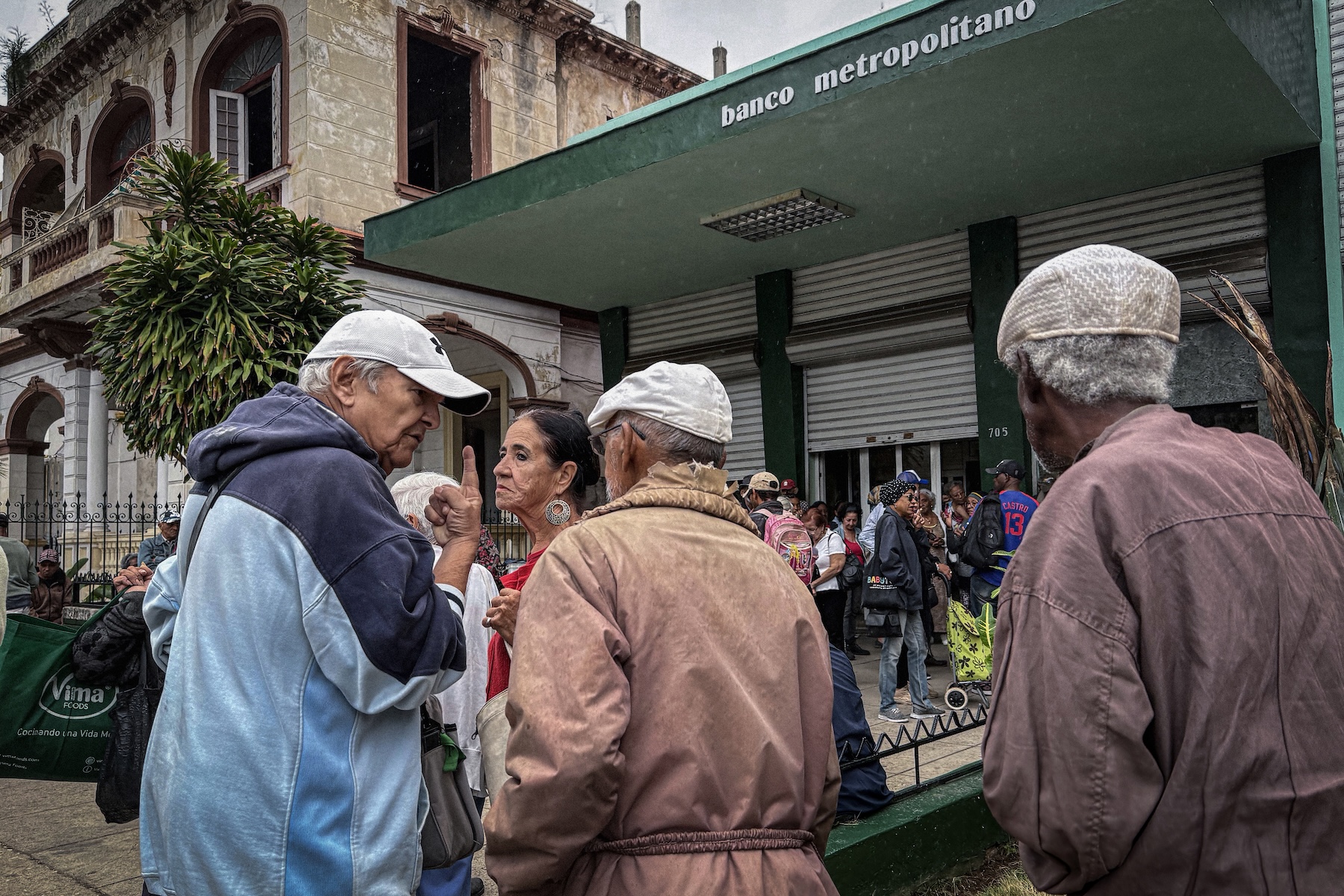 Photo of three elderly men at the back of the crowd in front of a bank building.