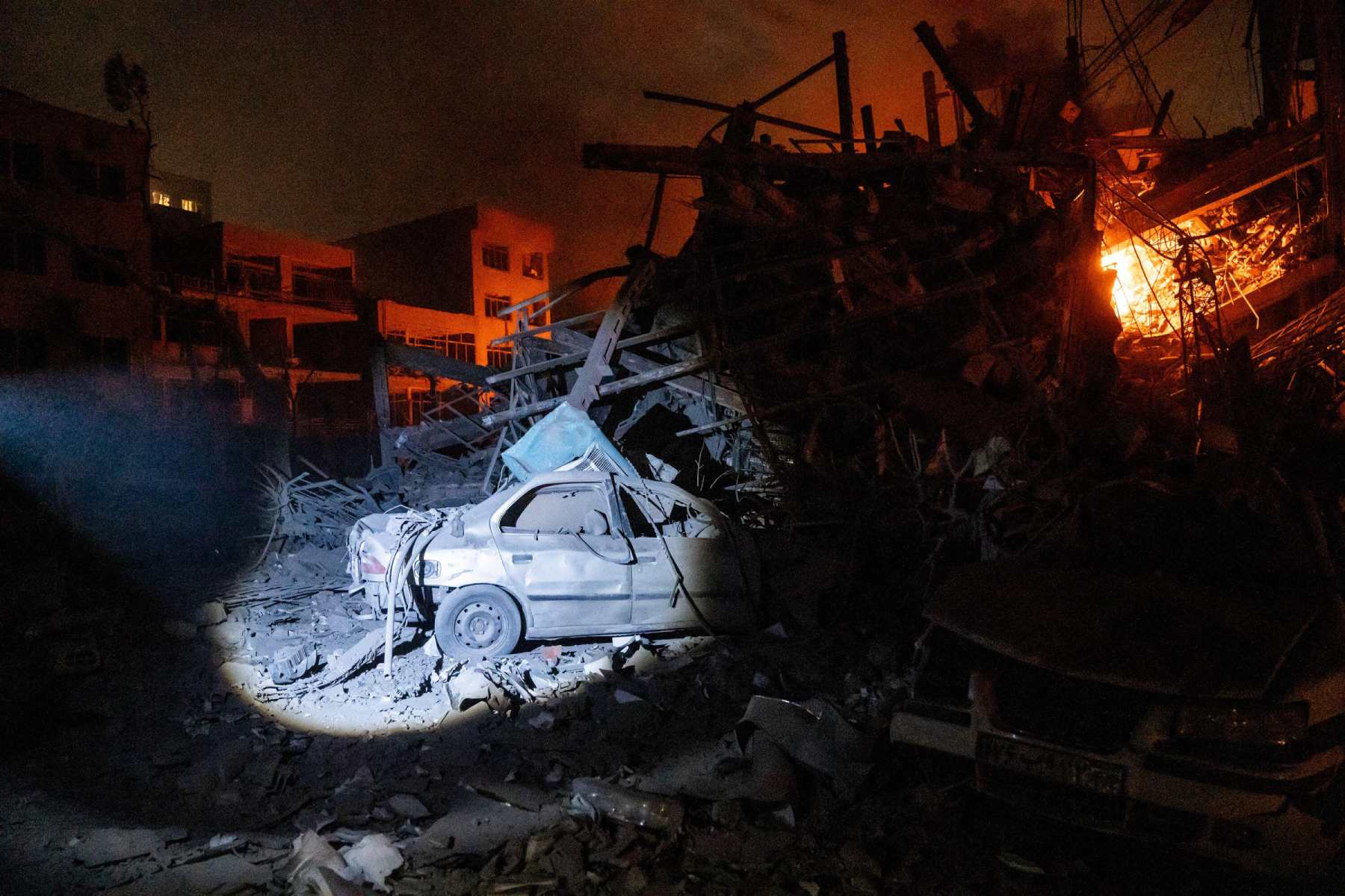 Photo of a car buried underneath a pile of rubble from a destroyed building in the dark.