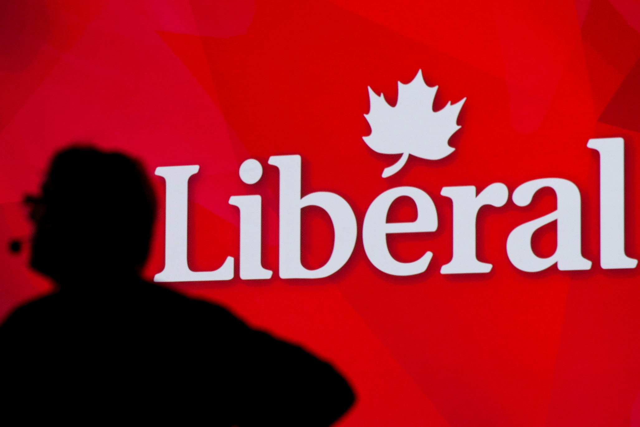 A man is silhouetted against a bright red background with Liberal spelled out in white.