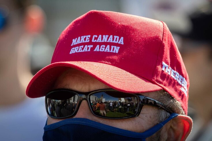 Close-up image of a man wearing sunglasses, a dark face mask, and a red cap that reads Make Canada Great Again.