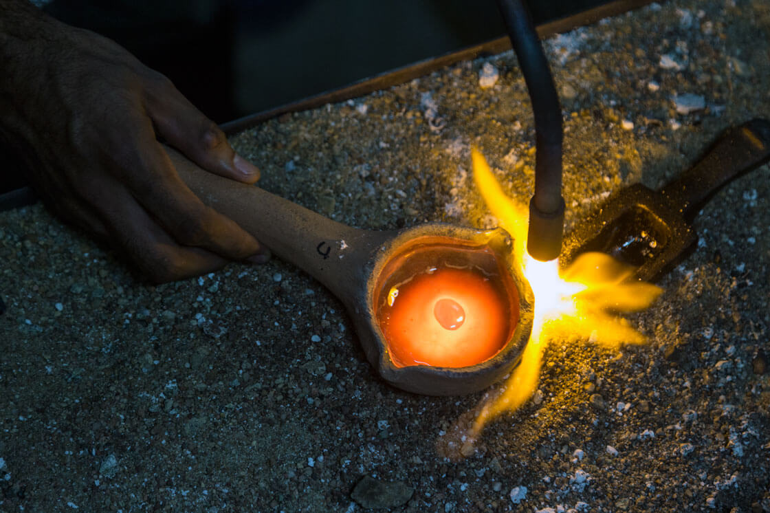 A closeup of a hand using a blowtorch to purify gold.
