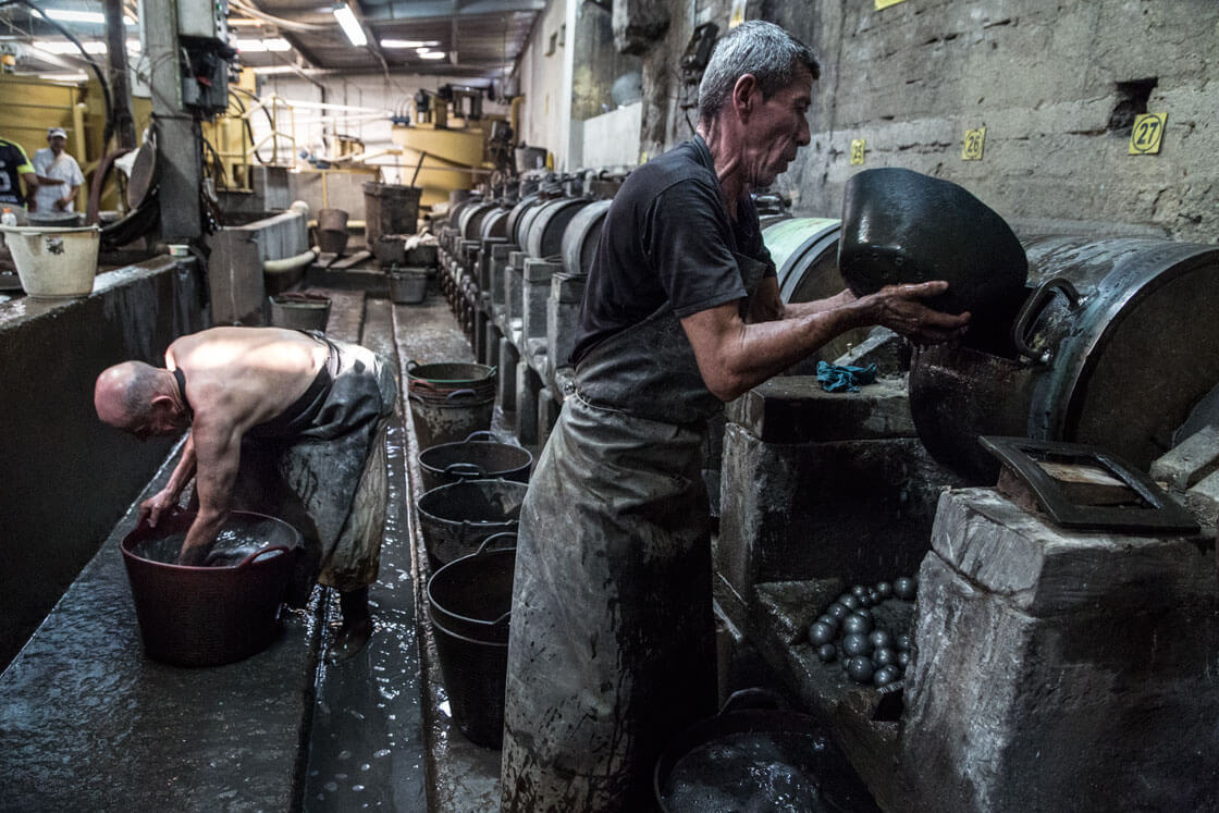 Two men  wearing aprons and working to separate gold from other material.