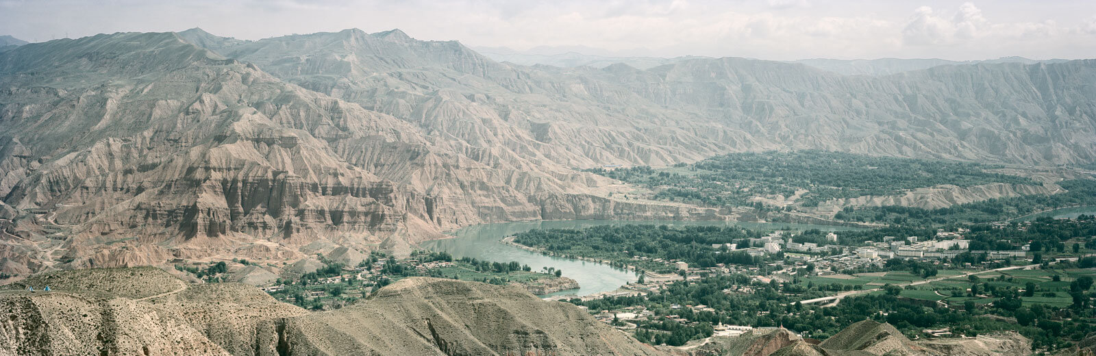 A panoramic shot of the town of Guide, which contains lush vegetation and is backed by huge mountains.