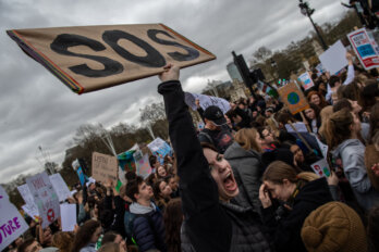 A woman protests at a climate change demonstration holding an "SOS" sign.