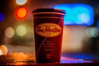 A close-up of a Tim Hortons cup with a dark background and bright lights behind it