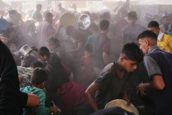 A photo of a dusty crowd of people holding pots and pans in the hopes of receiving food.