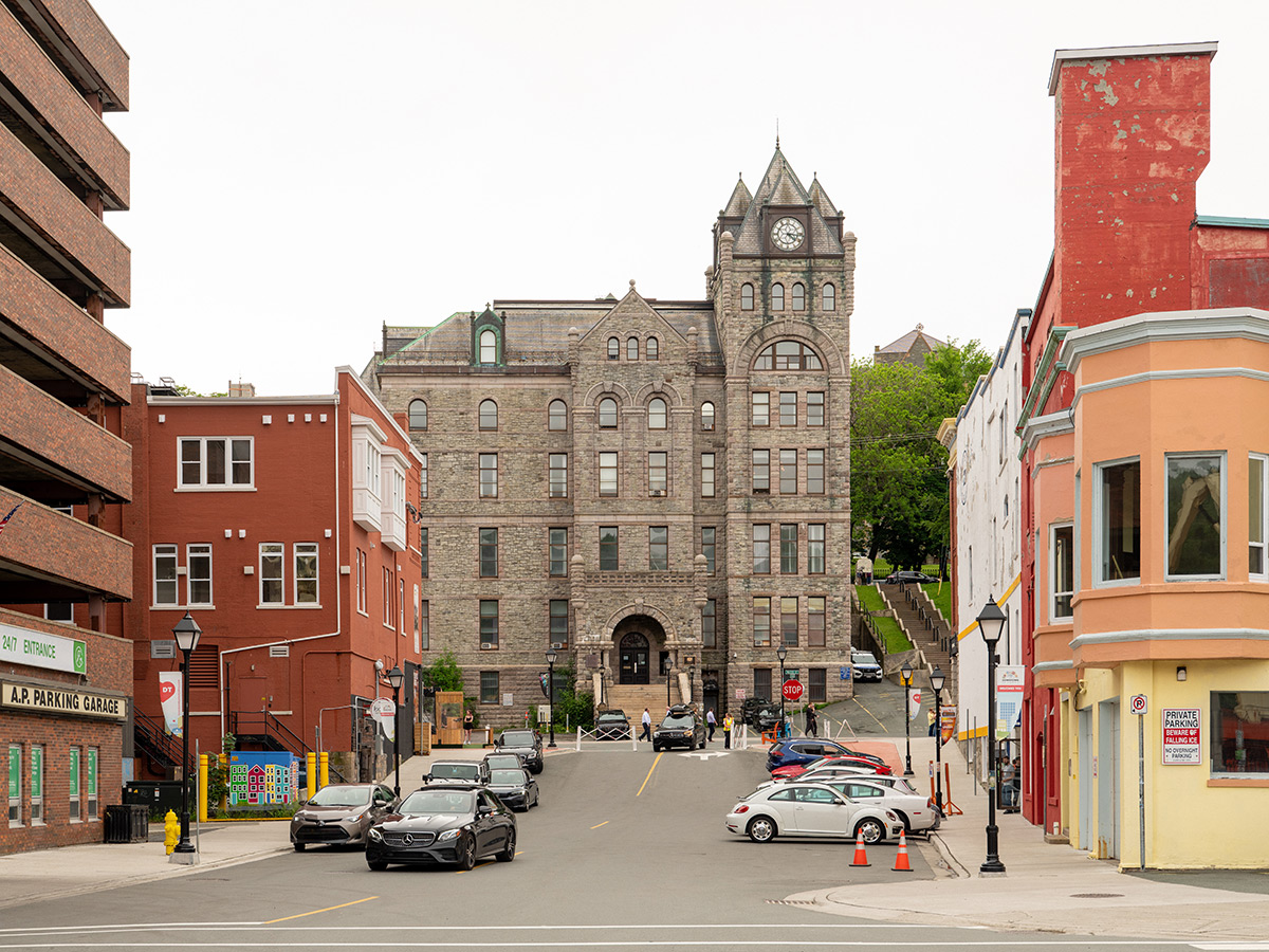 Streetview photo of the Supreme Court of Newfoundland and Labrador, a tall stone building in downtown St. John's, Newfoundland. Other buildings and parked cars are seen around the building.