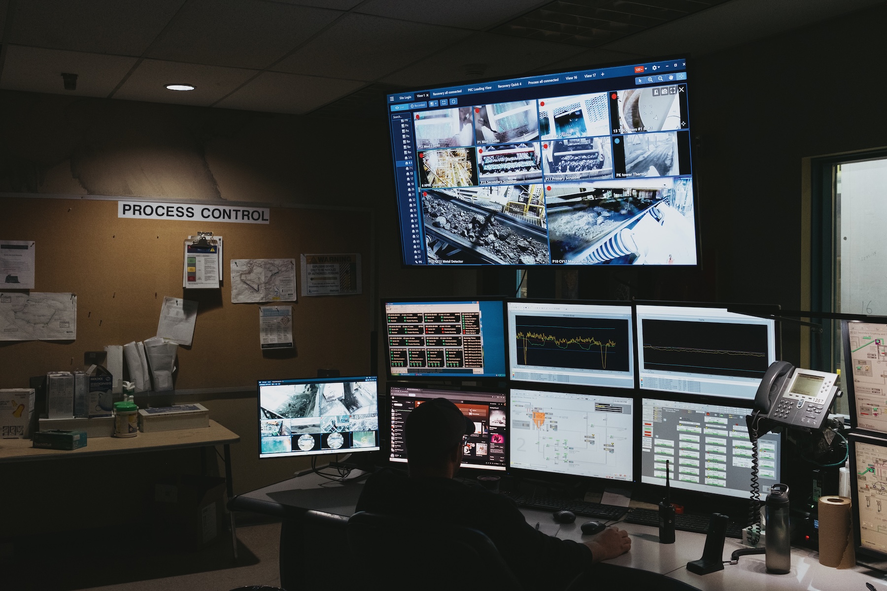 Photo of computer monitors at a desk. A sign on a cork board in the ...