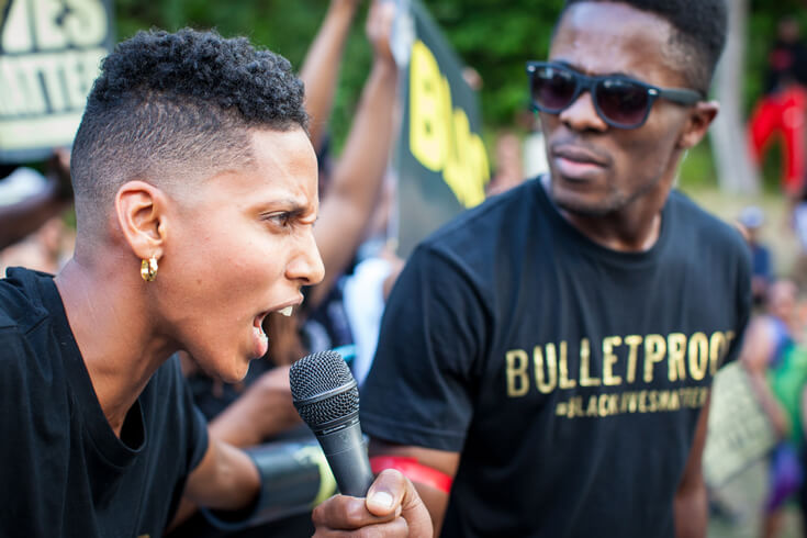 Janaya Khan, a leading organizer of Black Lives Matter Toronto, speaks into a microphone as a fellow protestor holds it up.