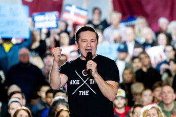 Pierre Poilievre, wearing an Axe the Tax t-shirt, speaks into a microphone at a rally