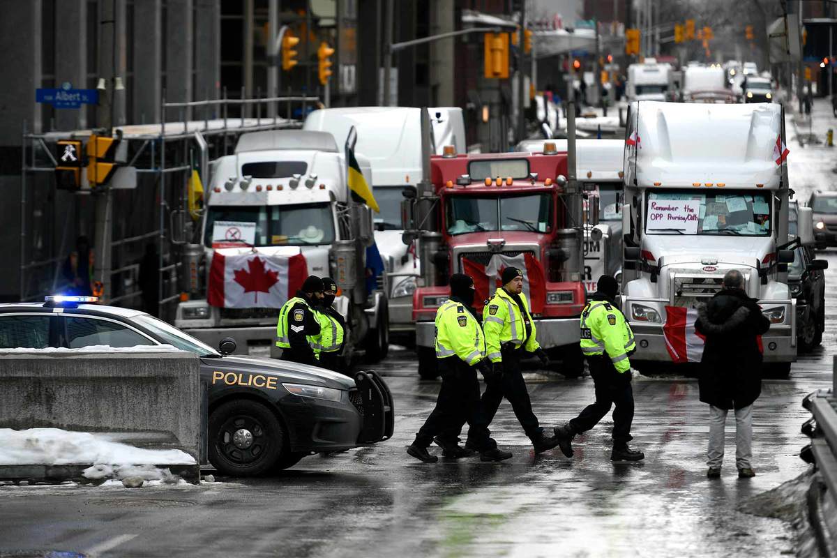 A photo of police officers patrolling on foot in front of three trucks with Canadian flags pinned on their fronts during a protest against COVID-19 restrictions where truckers flooded the streets of Ottawa in Feb. 2022.