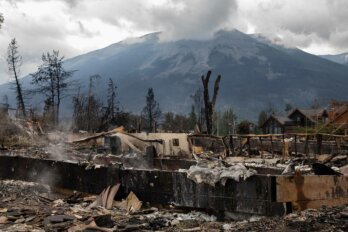 Jasper, Alberta, after the 2024 wildfire. A smoky mountain and cloudy sky provide a backdrop to the burned structures and trees