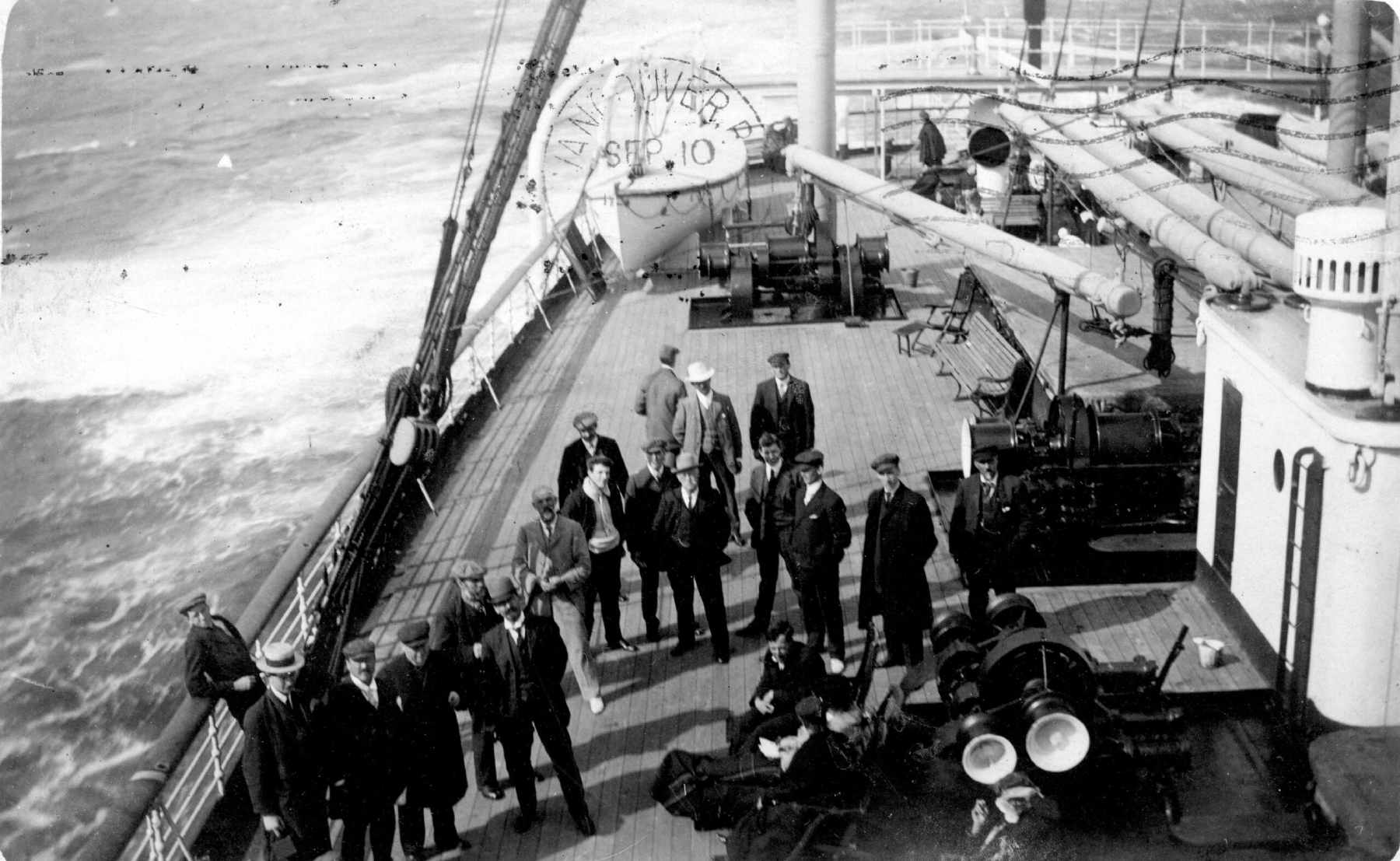 A black and white photo shows a group of men gathered on the deck of a ship