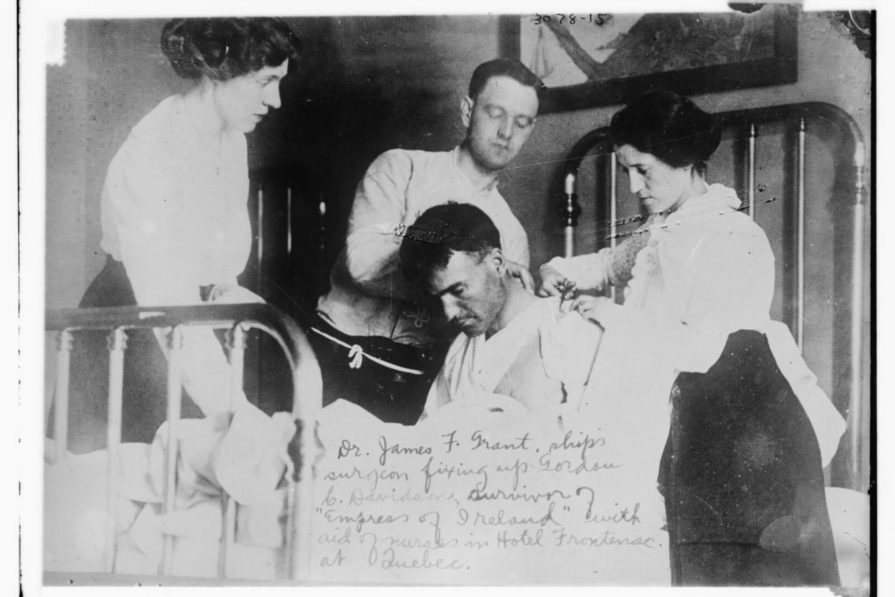 Black and white photo shows a man and two women attending to a male patient