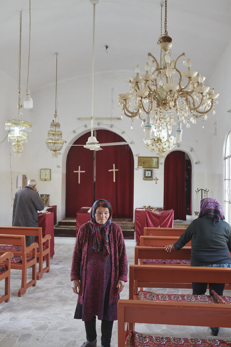 A woman facing the camera with her back to the altar in a Christian church. On either side of her are two people facing the altar and praying.