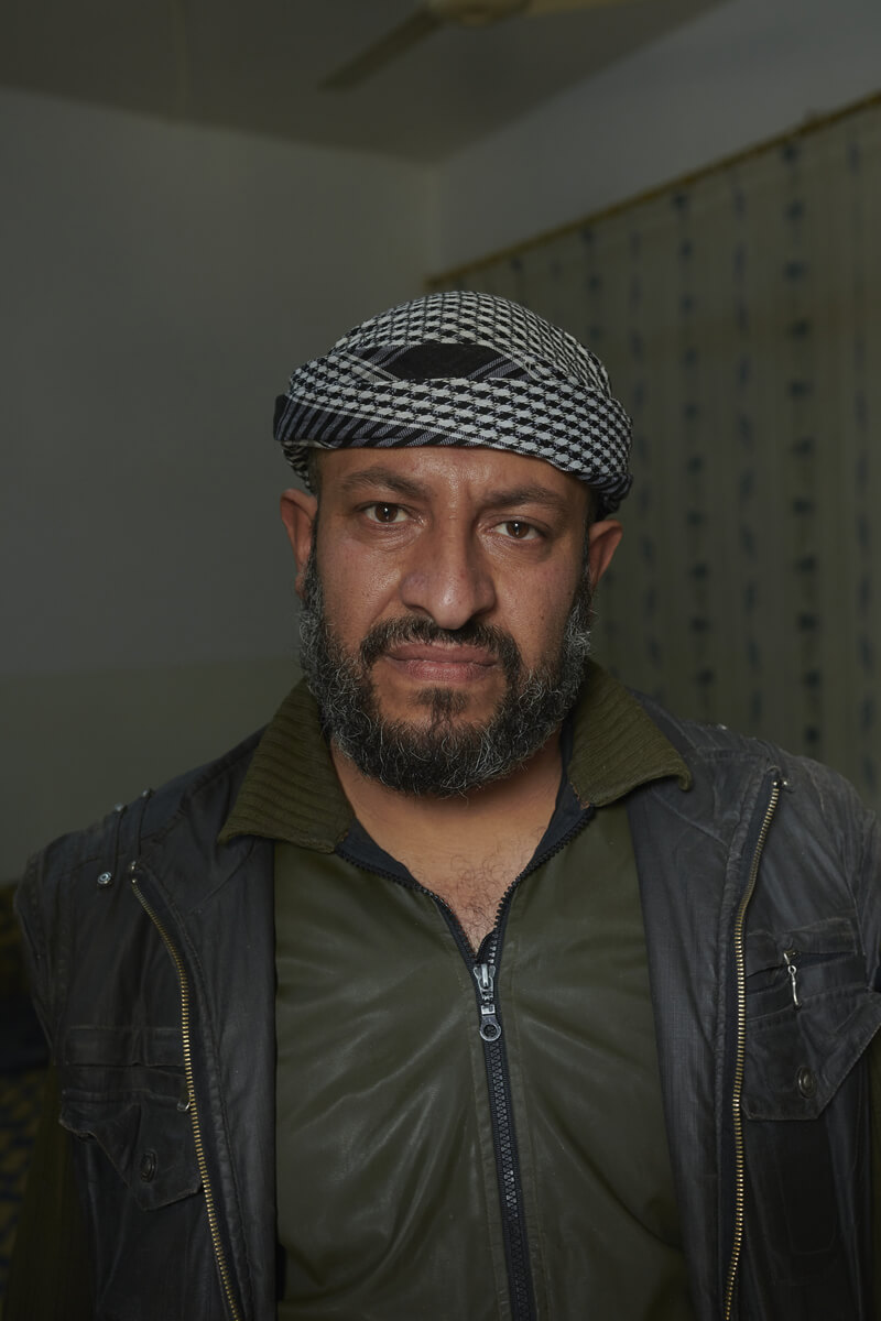 A closeup of a bearded man wearing a cap and looking into the camera.