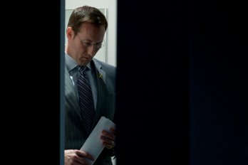 A photo of Peter MacKay framed by a partially open door. He is looking downward and carrying a sheaf of papers in his hand.