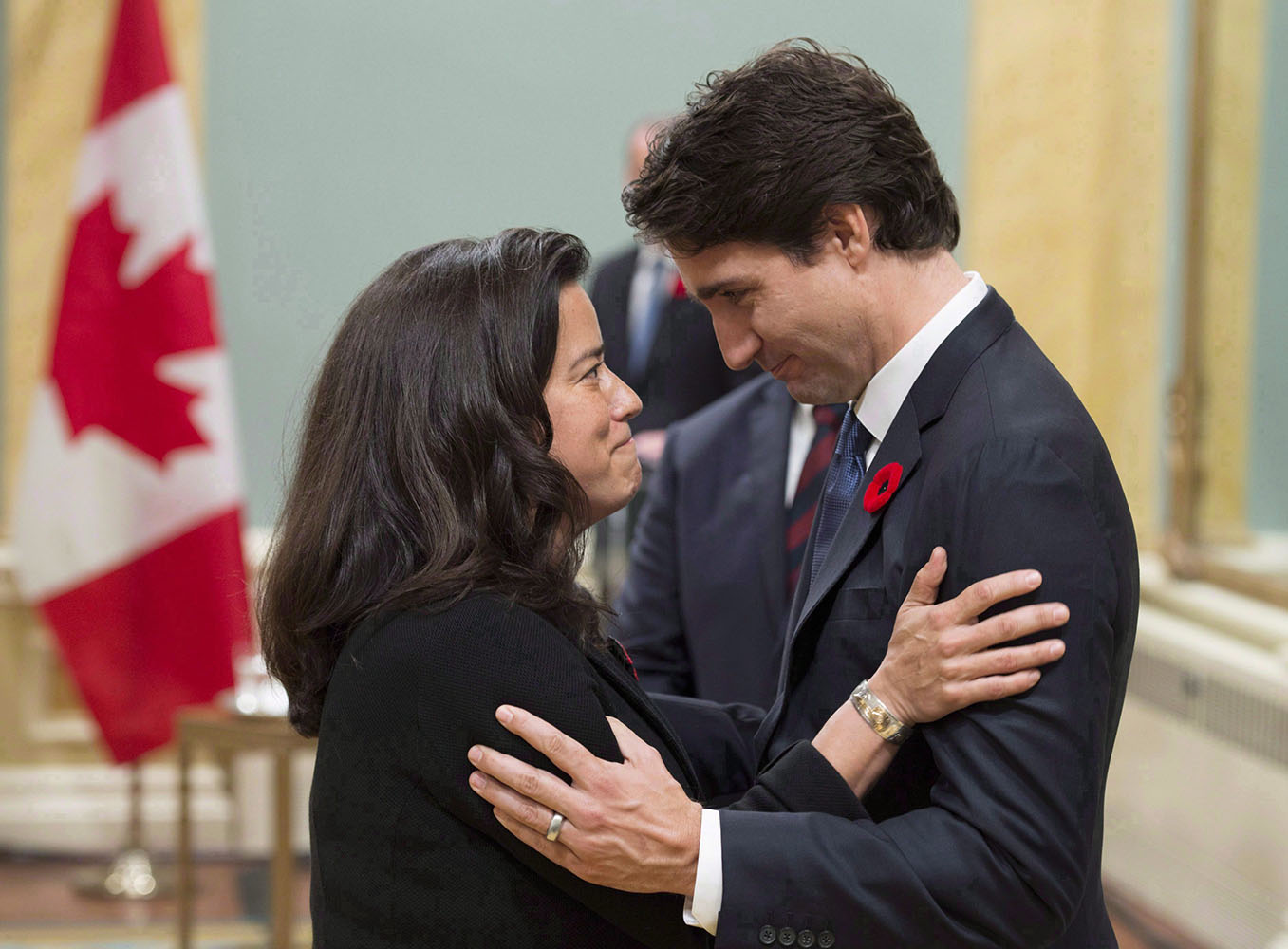 In Rideau Hall, Justin Trudeau and Jody Wilson-Raybould face each other and smile while standing close and holding onto each other's upper arms.
