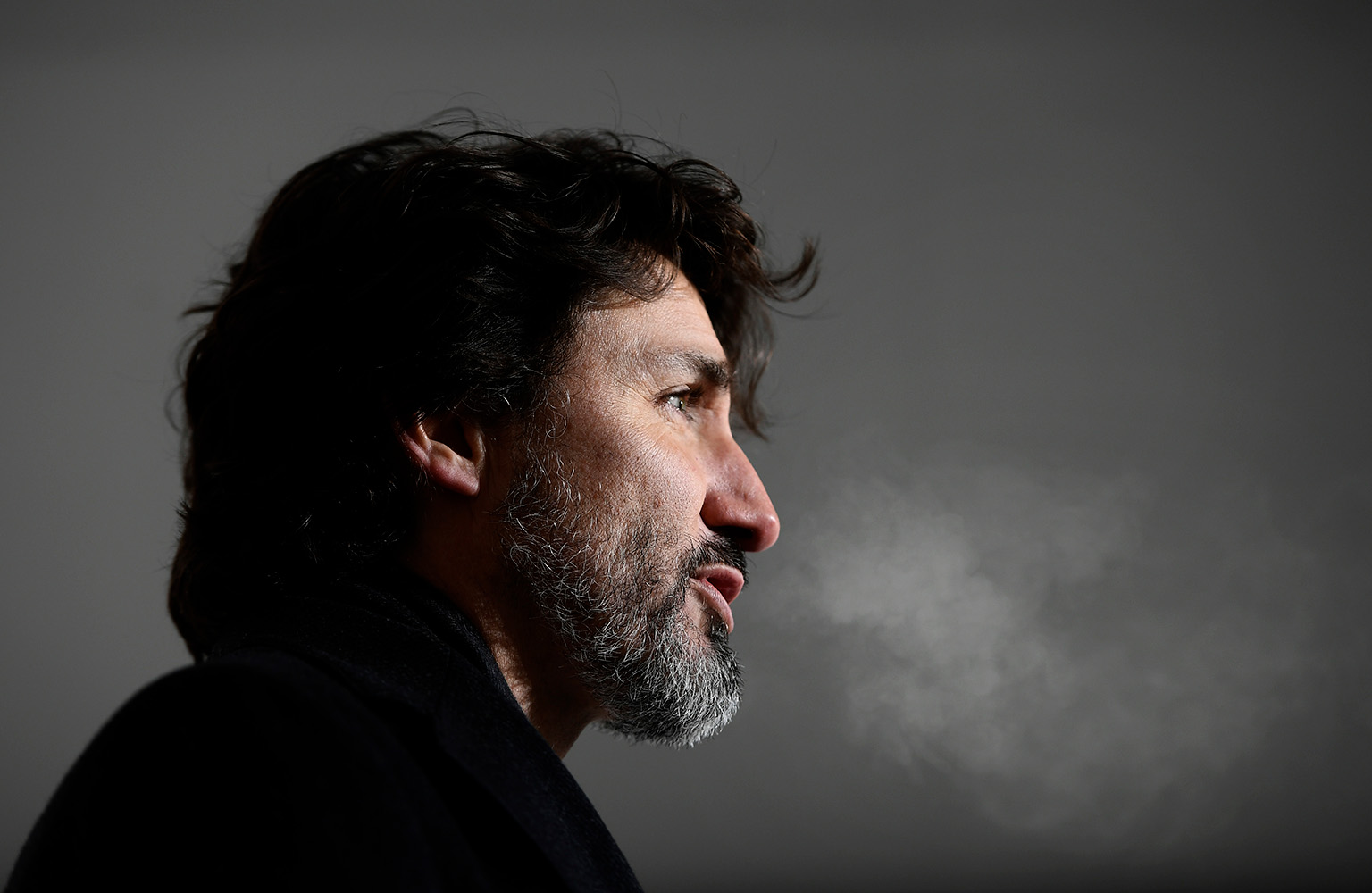 Justin Trudeau stands outside at night, his breath visible in the cold. He has longer hair and a beard.