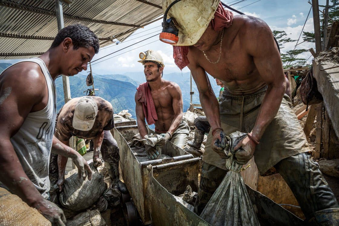 Several miners hoist heavy bags of material at the opening of a mining shaft.