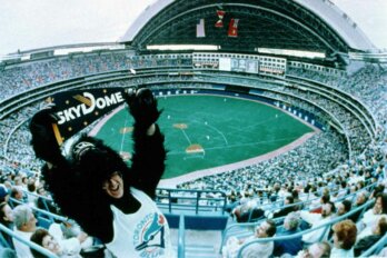 A photo of the first Blue Jays game played at Skydome. In the foreground, a man dressed as a gorilla is holding a sign that reads SkyDome.