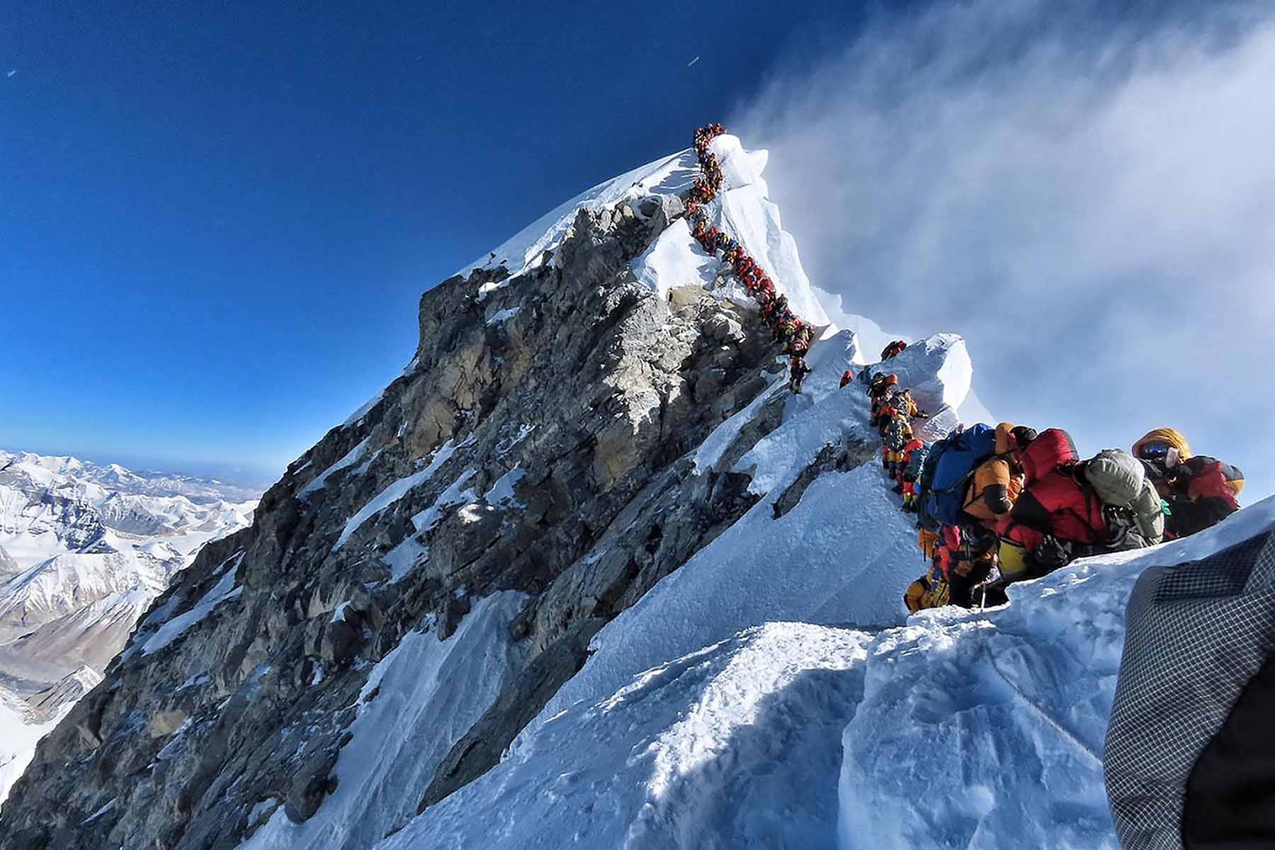 Hikers with brightly coloured coats and packs scale the snowy peak of Mount Everest in single file.